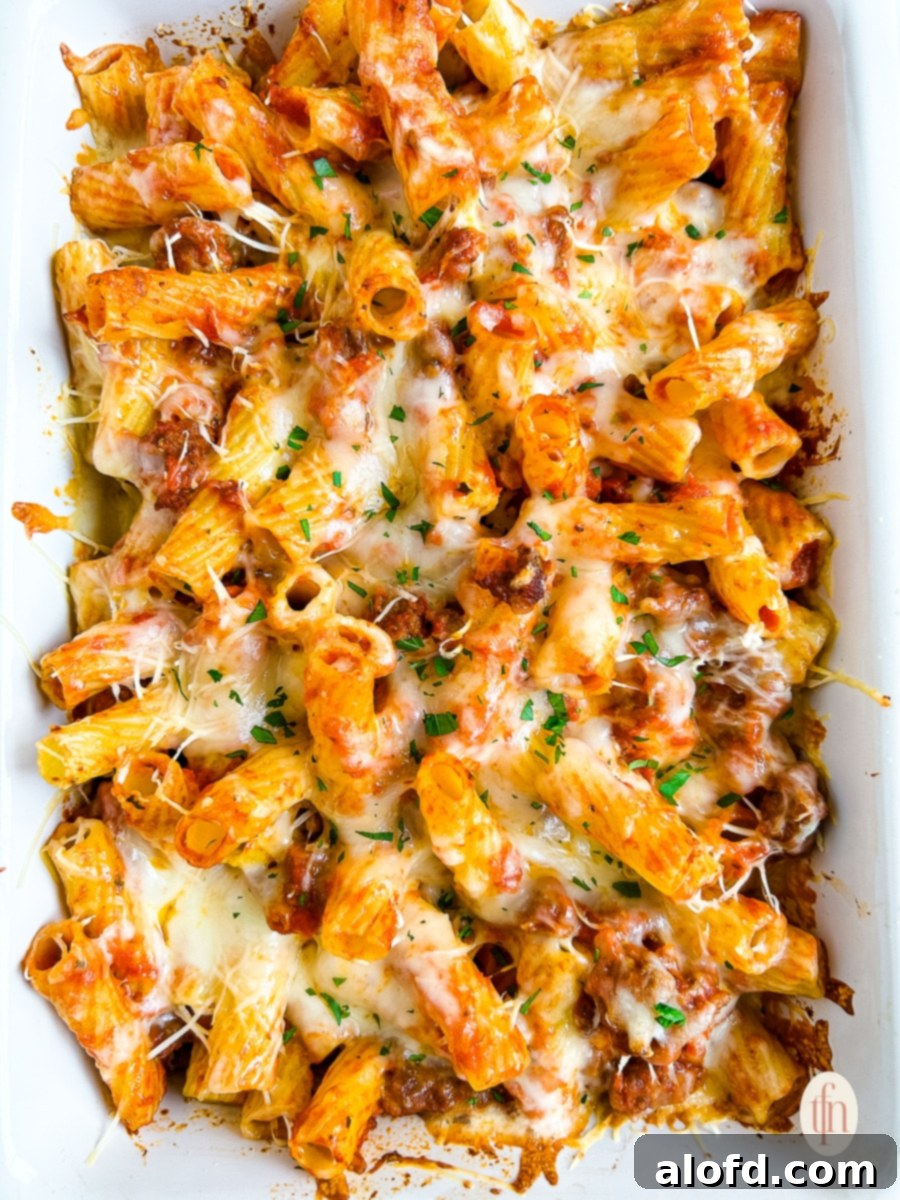 Baked rigatoni with sausage, garnished with fresh basil, ready to serve in a white casserole dish.