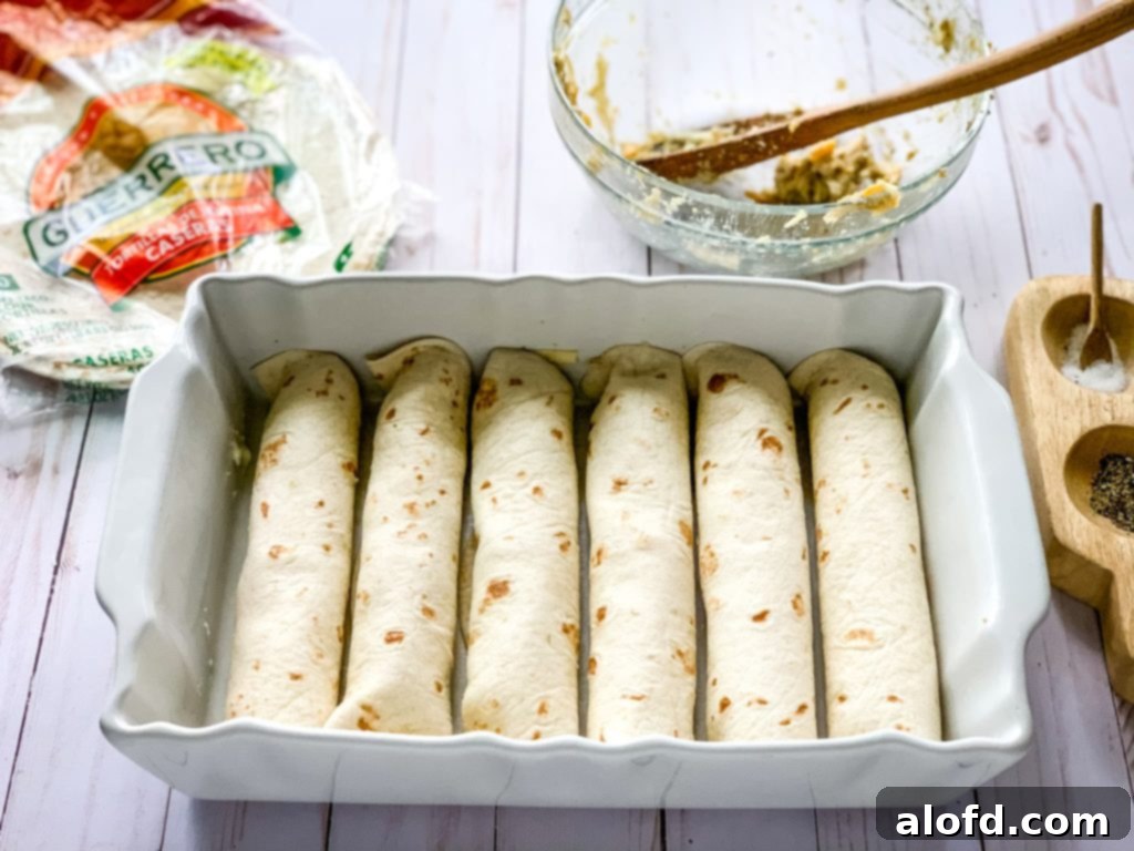 Luscious Sour Cream Chicken Enchiladas 9 Prepping chicken enchiladas in a white baking dish.