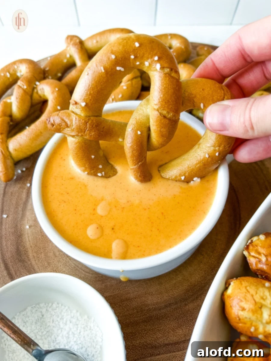 Hand dipping pretzel into rich, golden pretzel cheese sauce, showcasing its creamy texture.