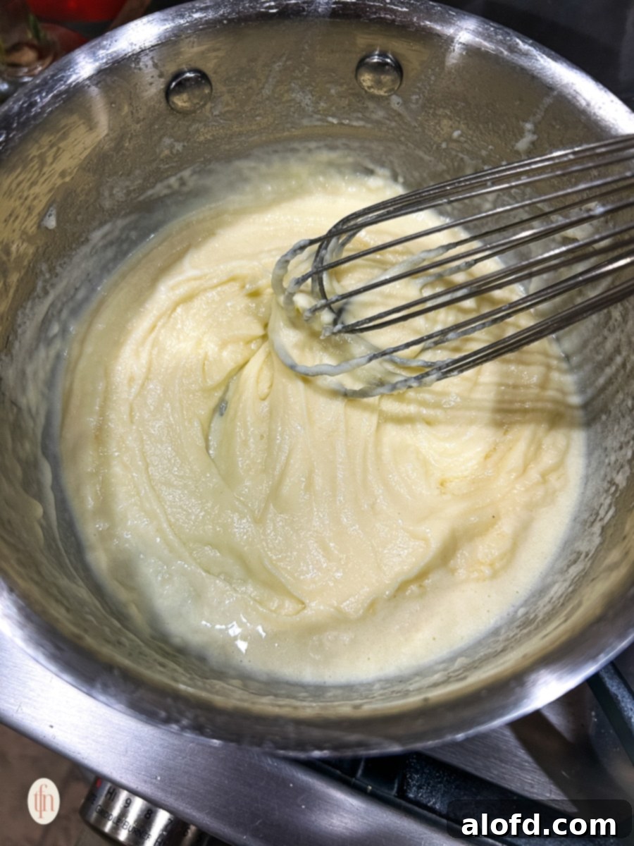 A whisk smoothly combining butter, flour, and liquid in a saucepan, demonstrating the early stages of sauce preparation.