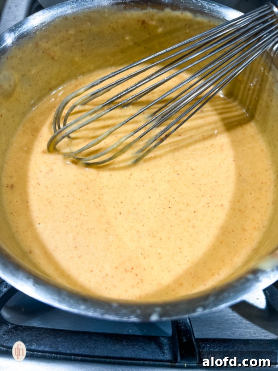 A whisk stirring up the creamy, golden pretzel cheese sauce in a saucepan, ensuring a smooth consistency before serving.