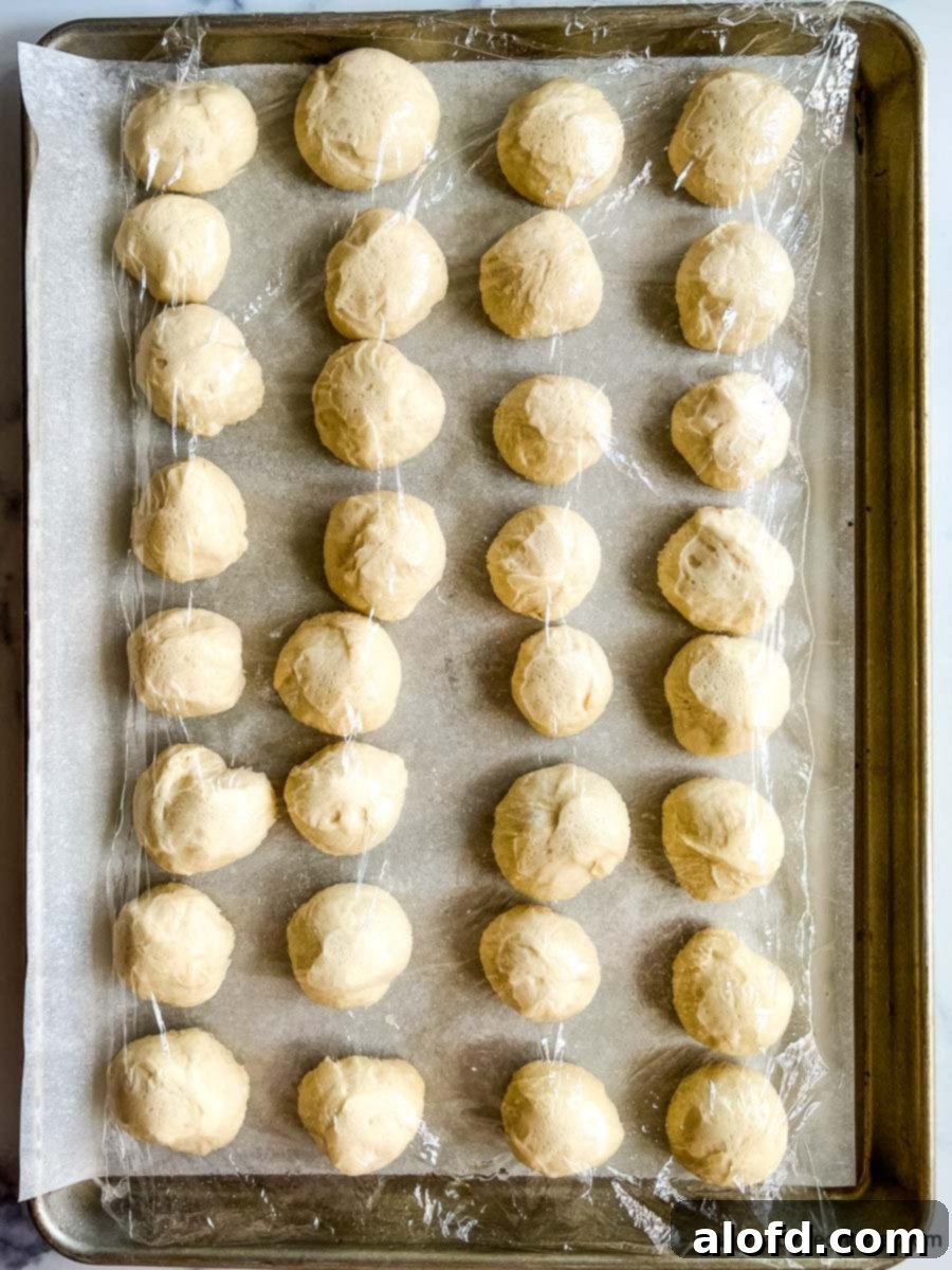 Pretzel Poppers 7 A sheet of rising bread dough balls covered with plastic wrap.