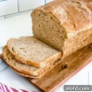 a square photo of a slice whole wheat sourdough sandwich bread on top of a wooden board.