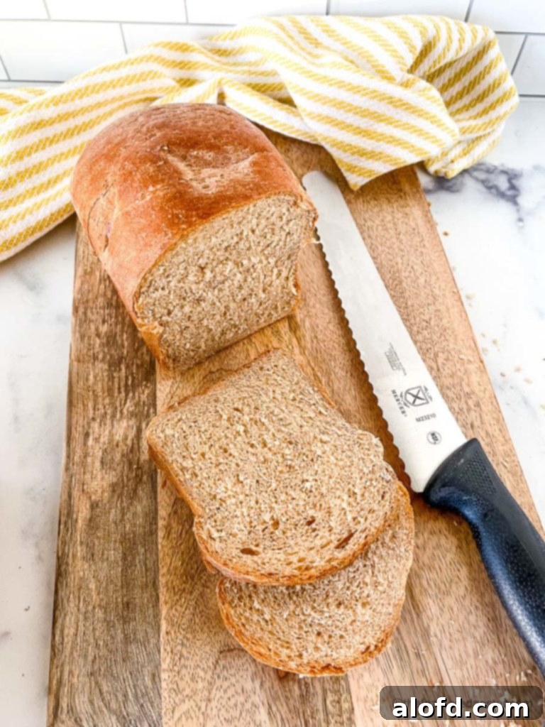 A freshly baked loaf of sliced whole wheat sandwich bread displayed on a rustic bread board, accompanied by a sharp bread knife and a yellow and white kitchen towel, ready for enjoyment.