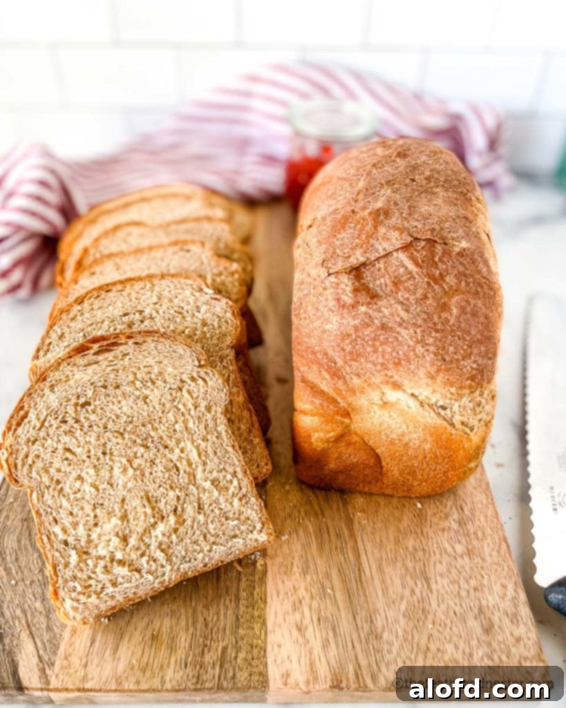 Two golden-brown loaves of whole wheat sandwich bread, one perfectly sliced to reveal its soft texture and the other whole, showcasing the rich crust.