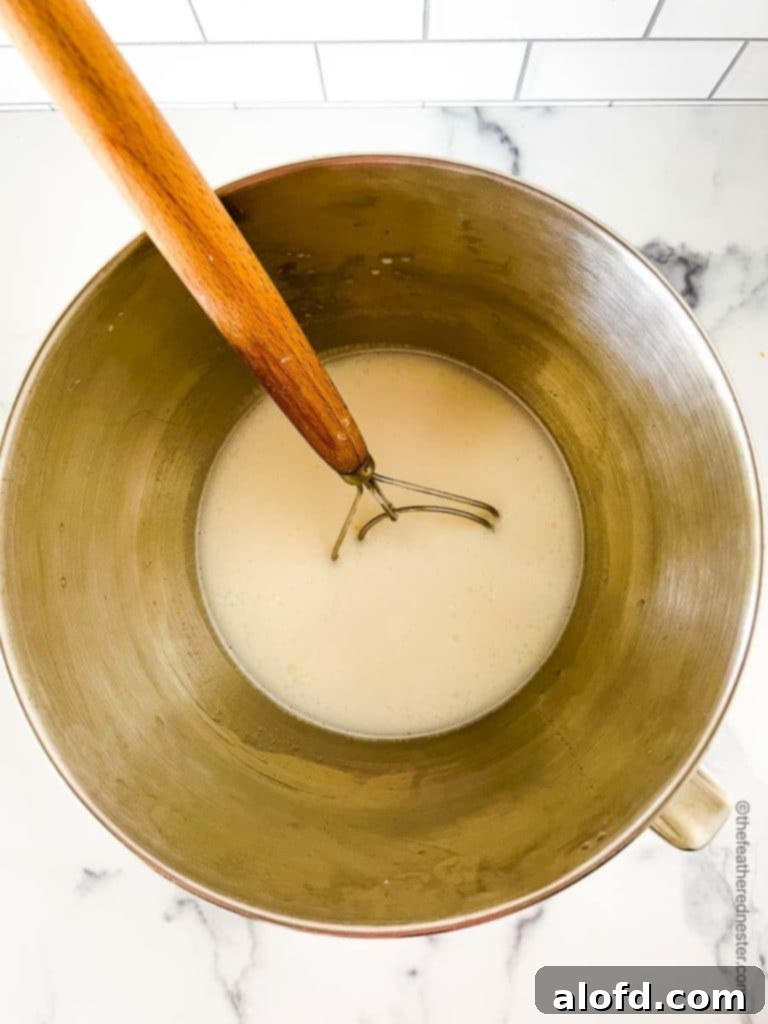 A stainless steel mixing bowl filled with the initial liquid ingredients—milk, water, and sugar—ready for yeast activation in the process of making whole wheat bread dough.