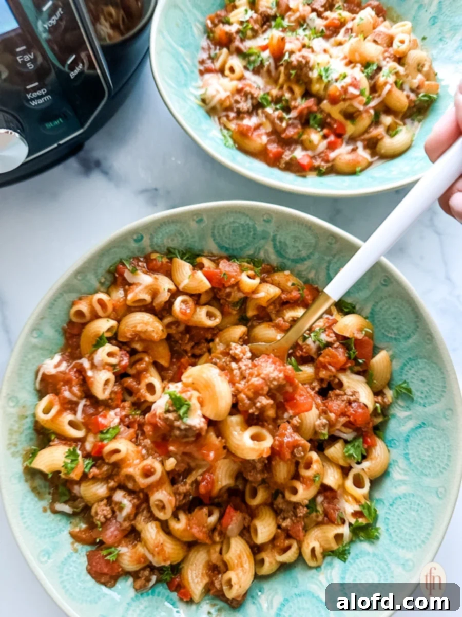 A serving spoon lifting a spoonful of rich, cheesy Instant Pot Chili Mac from a bowl.