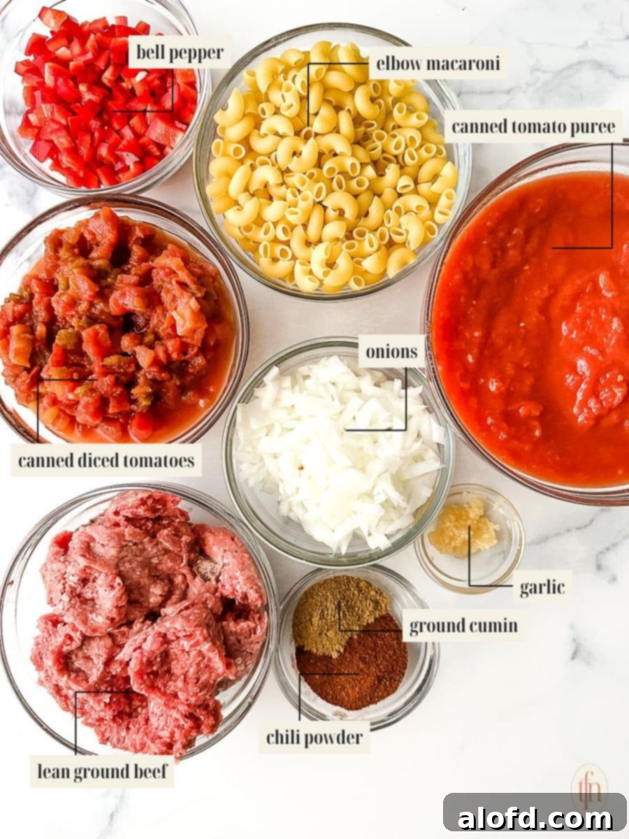 Carefully arranged ingredients for a chili mac recipe, including ground beef, diced vegetables, and pasta.