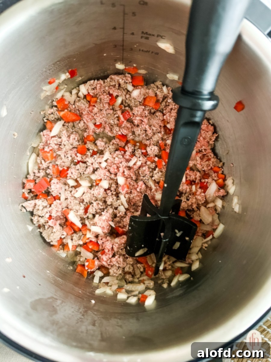 Browning ground beef with diced tomatoes, onions, and spices in a large pot, forming the base of the chili mac.