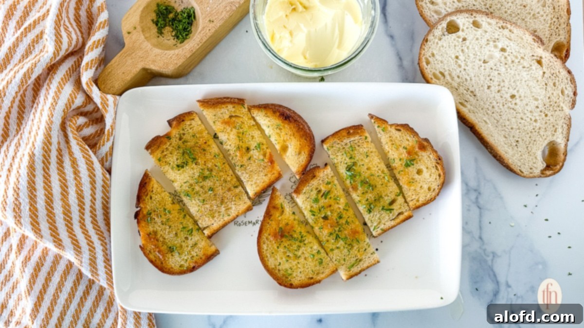 Two perfectly toasted slices of homemade sourdough garlic toast, golden brown with visible garlic bits, served on a white plate next to fresh herbs and a small bowl of butter.