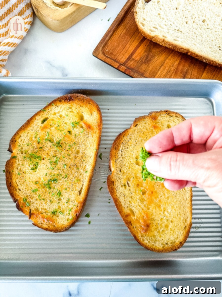 Freshly toasted sourdough garlic bread slices sprinkled with vibrant green chopped parsley, presented beautifully on a white plate, adding a fresh garnish.