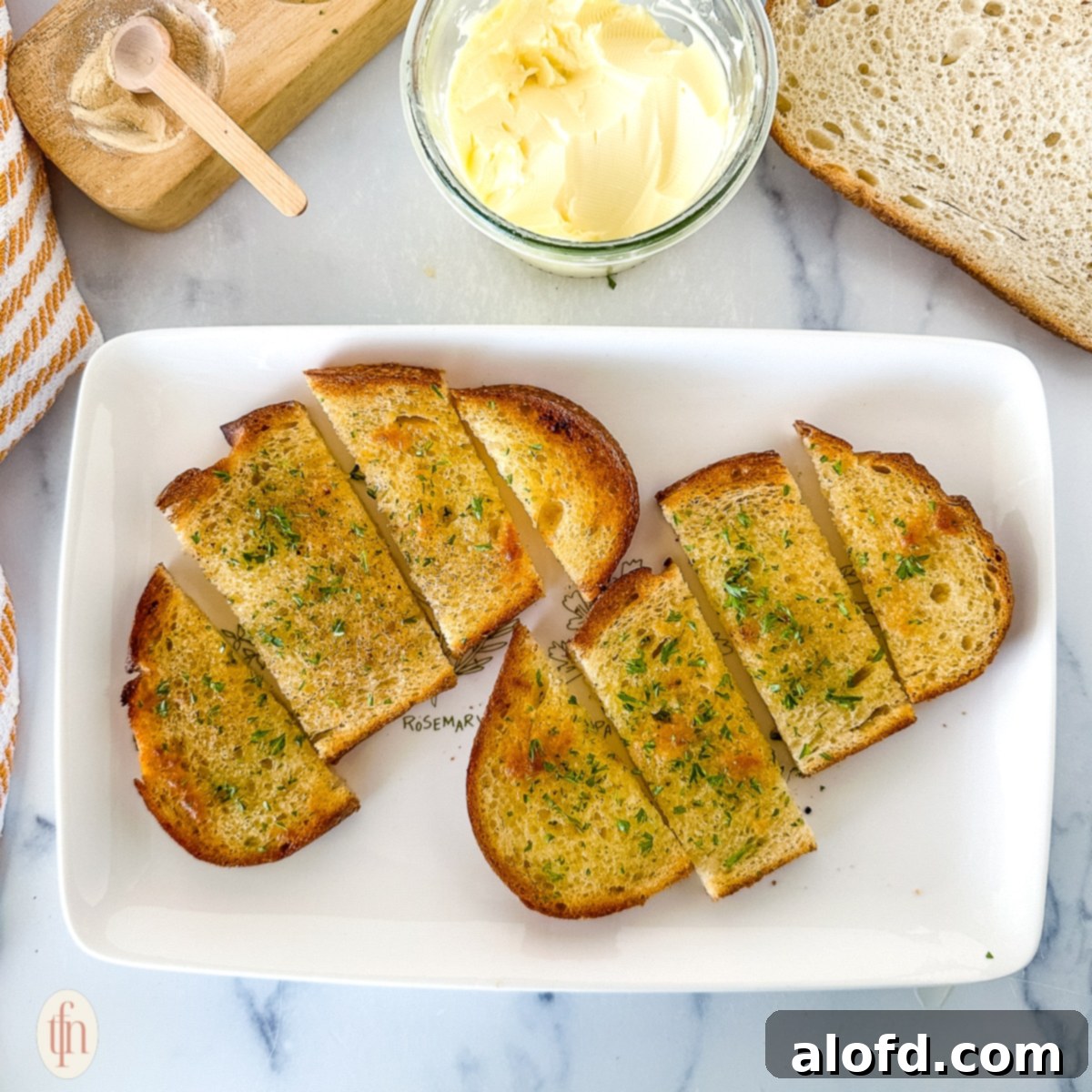 Two generous slices of golden-brown sourdough garlic toast, adorned with fresh herbs, resting on a white plate next to a small bowl of butter and additional garnishes.