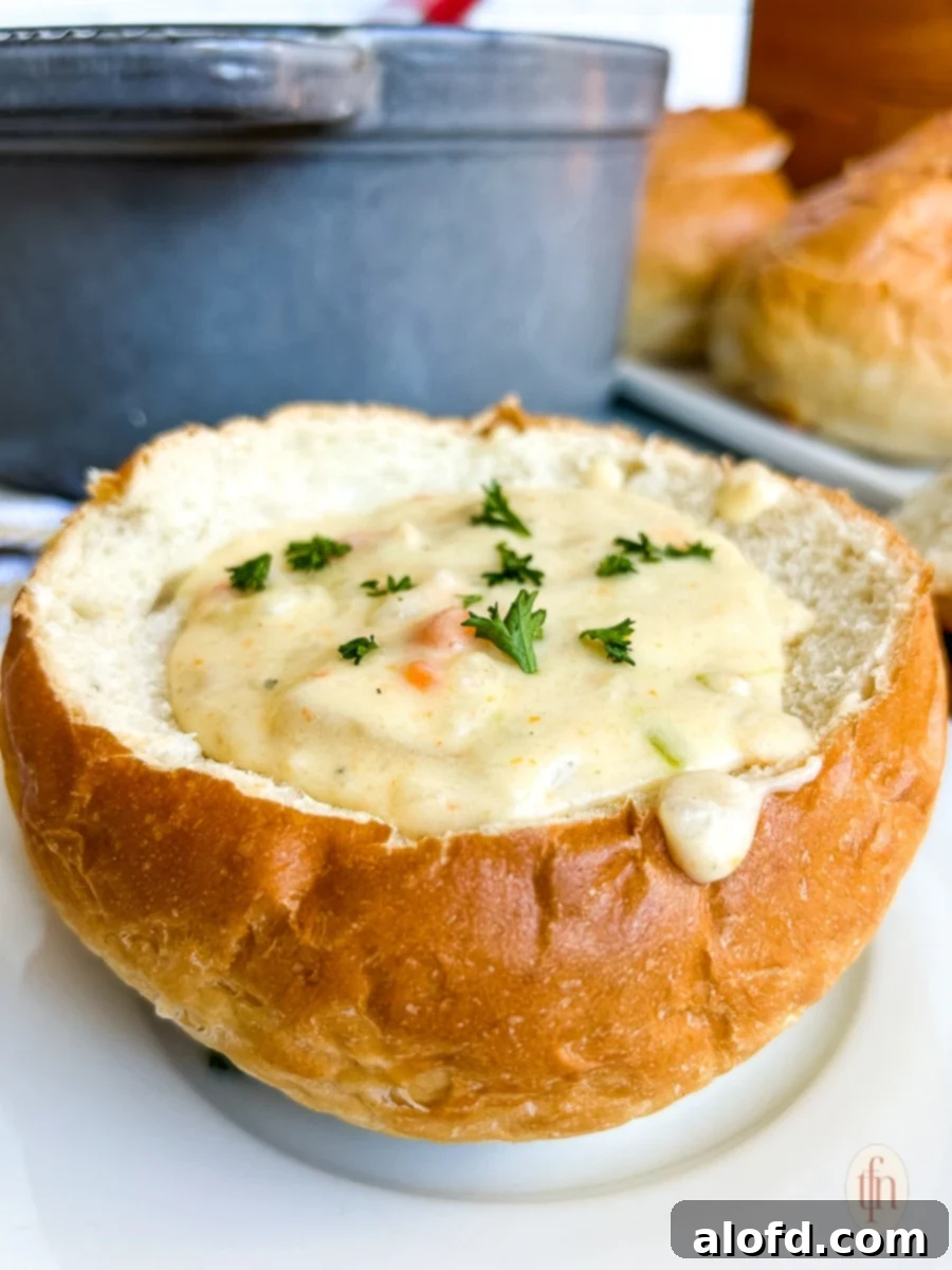 Close up of San Francisco Clam Chowder in a bread bowl on a white plate, garnished with fresh parsley.