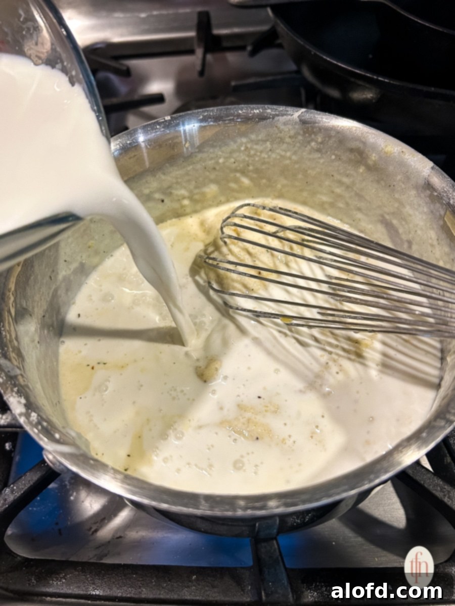 Pouring milk into a mixture of flour and butter (roux) on a stovetop.