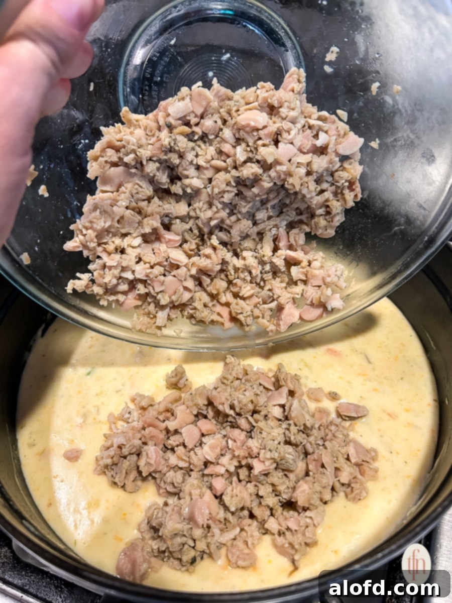 Pouring drained clams into the simmering soup mixture on the stovetop.