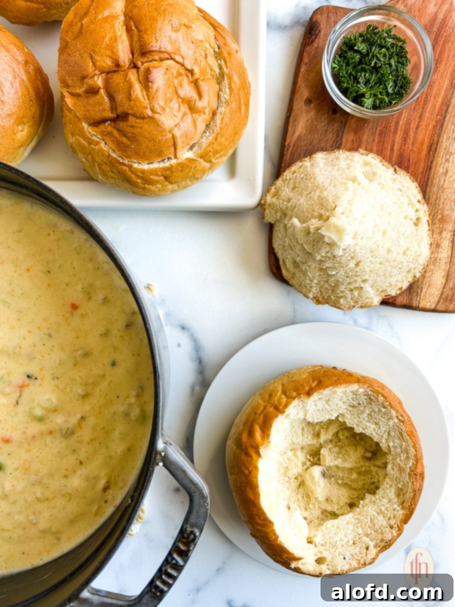 An empty sourdough bread bowl sits next to a pot of creamy clam chowder.