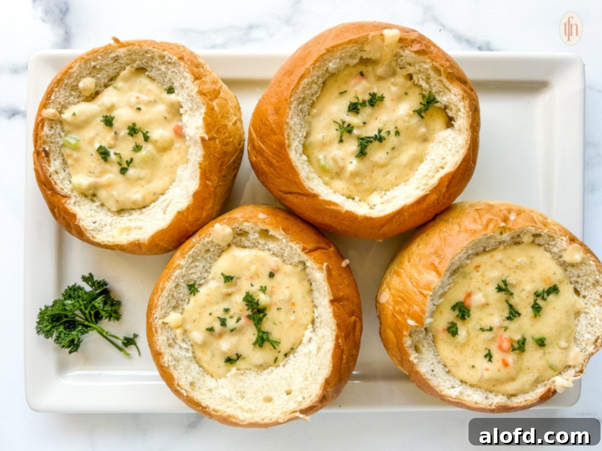 Two servings of San Francisco clam chowder in bread bowls arranged on a white platter, garnished with fresh herbs.