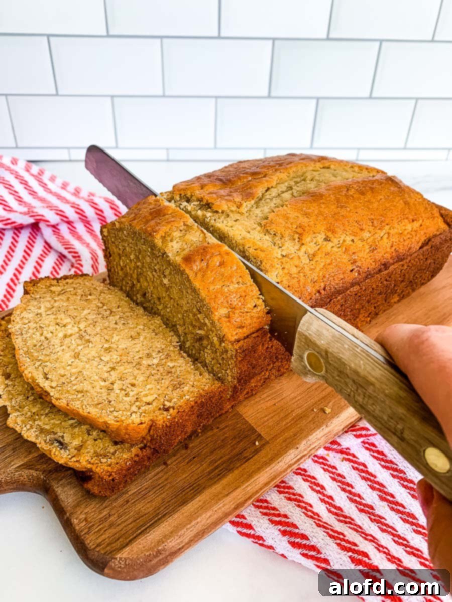 Effortless Self-Rising Banana Bread 9 slicing banana bread self rising flour on a wooden board with a red and white kitchen towel.