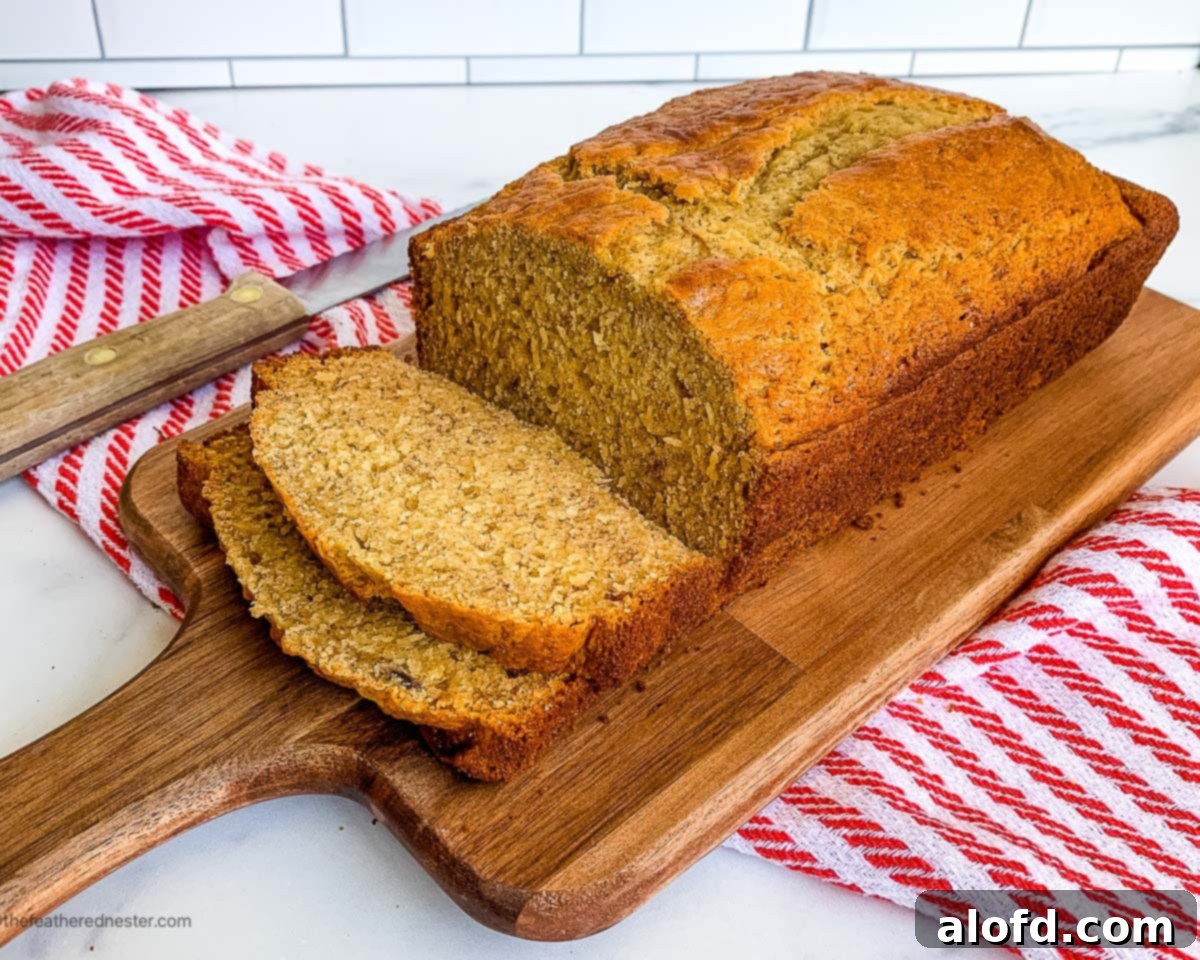 Effortless Self-Rising Banana Bread 10 A loaf of sliced banana bread recipe with self rising flour on a wooden board with a red and white kitchen towel.