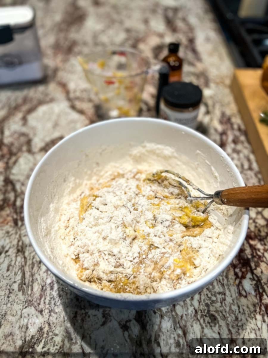 A close-up shot of dry ingredients being added to a banana bread mixture in a large mixing bowl, illustrating the combining step.