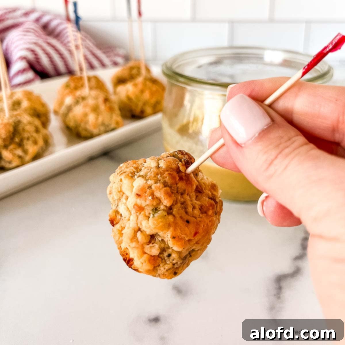 A skewered pimento cheese sausage ball with a tray of more appetizer balls in the background.
