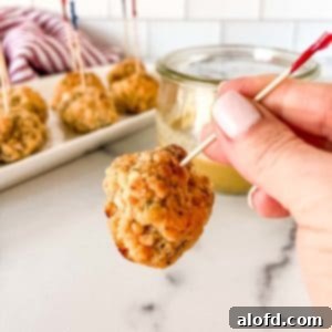 A skewered pimento cheese sausage ball with a tray of more appetizer balls in the background.