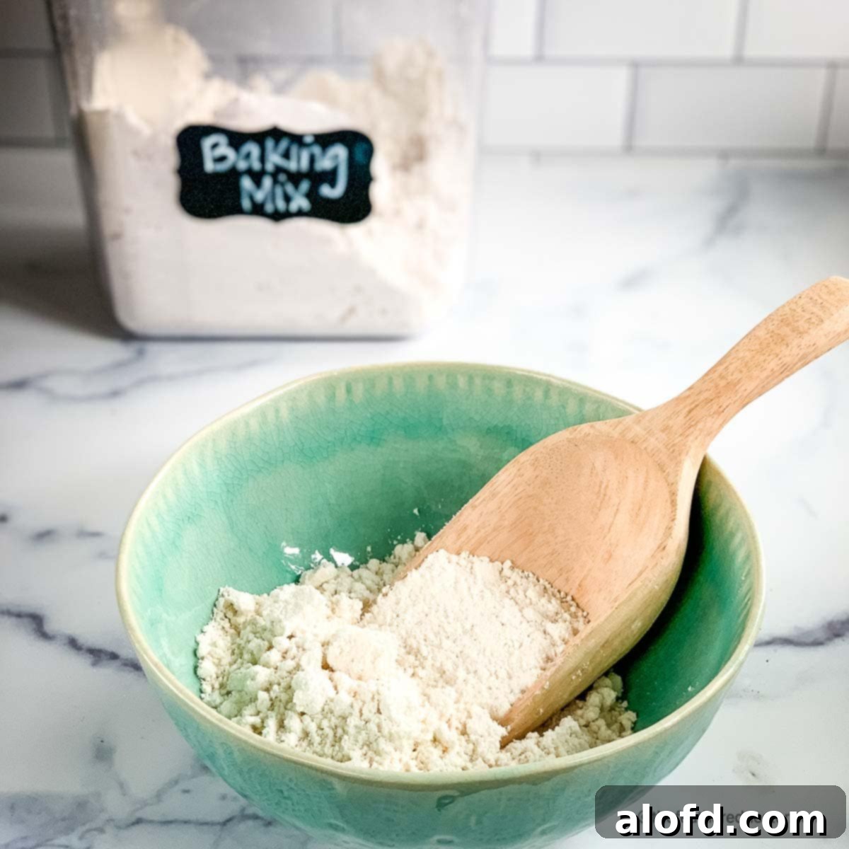 A green bowl of homemade baking mix with a container of it in the background.