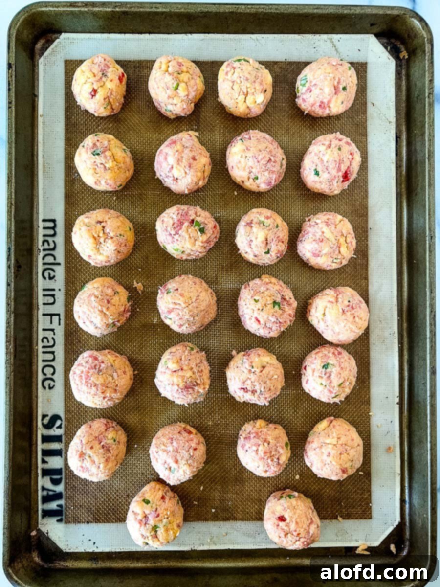 A baking sheet with unbaked pimento cheese sausage balls, ready for the oven.