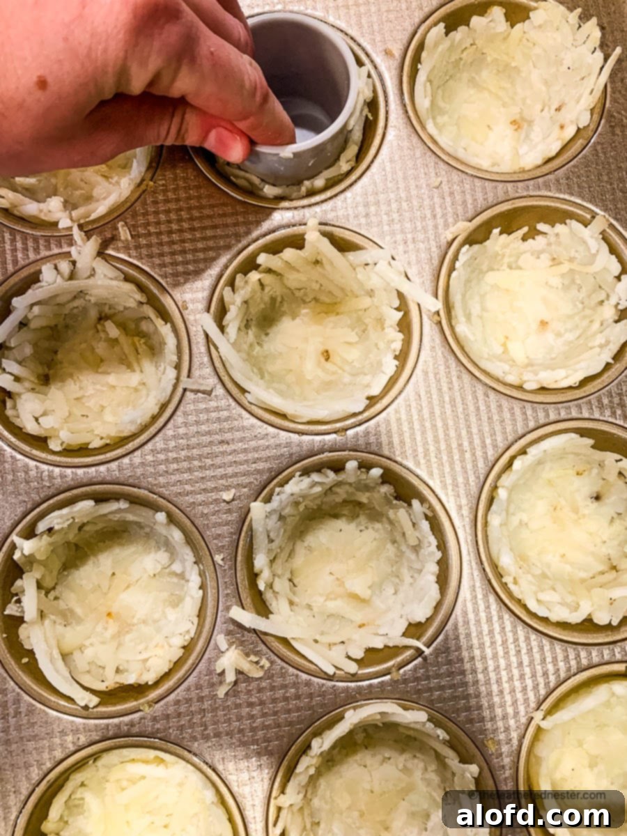 Crispy Hash Brown Egg Cups 7 Using a shot glass to press hash browns into muffin tins so they look like birds nests.
