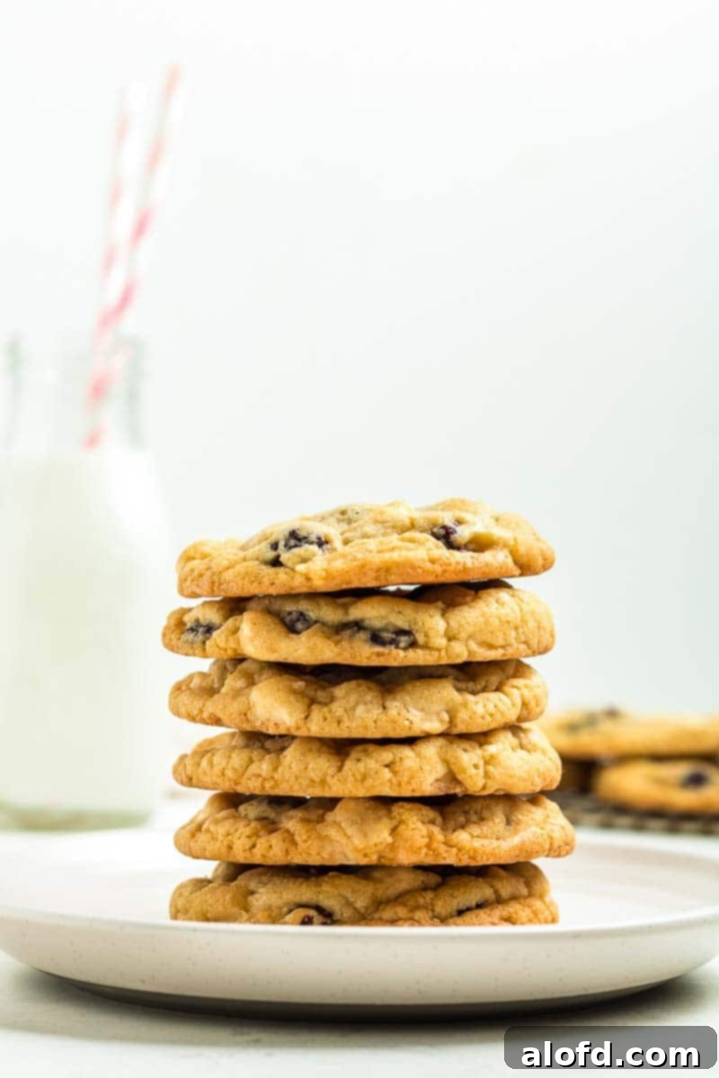 A stack of luscious white chocolate raspberry cookies, with a bottle of milk and straw in the background, inviting you to indulge.