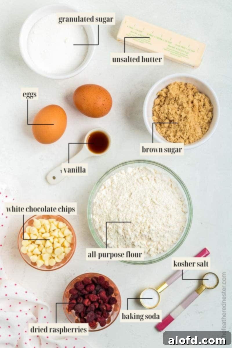 Bowls filled with granulated sugar, brown sugar, all-purpose flour, dried raspberries, and white chocolate chips, surrounded by fresh eggs, butter, and measuring spoons, ready for baking.