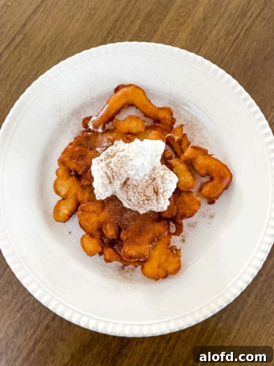 A white plate showcasing a homemade funnel cake generously topped with whipped cream and a sprinkle of cinnamon powder.