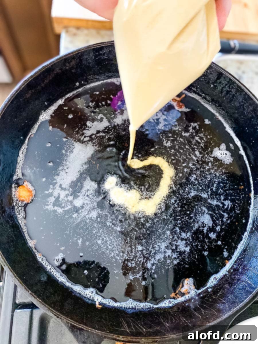 A Ziplock piping bag being used to pour Bisquick funnel cake batter in a circular motion into hot oil, forming a classic funnel cake shape.