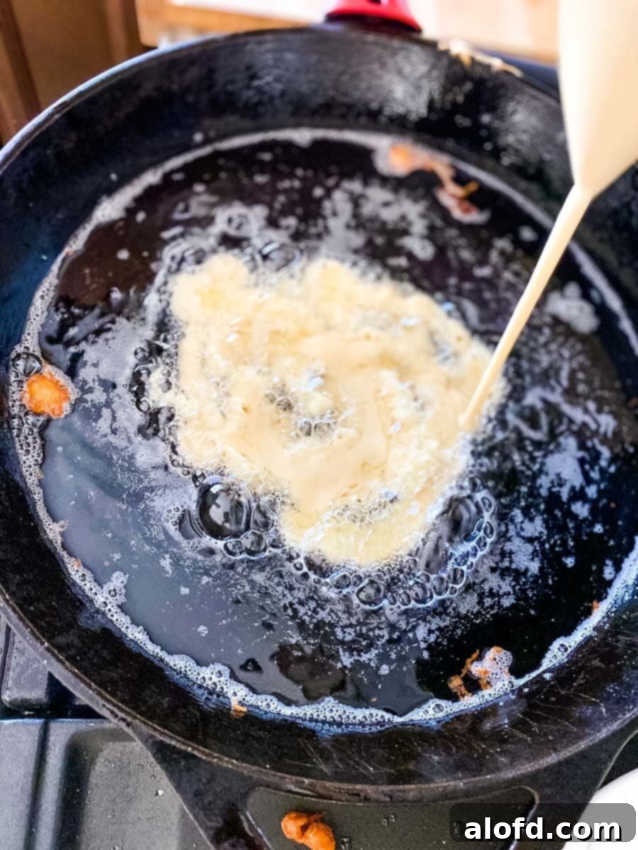 Close-up shot of Bisquick funnel cake batter being squeezed in a circular pattern into hot oil, creating a delicate, lace-like structure.
