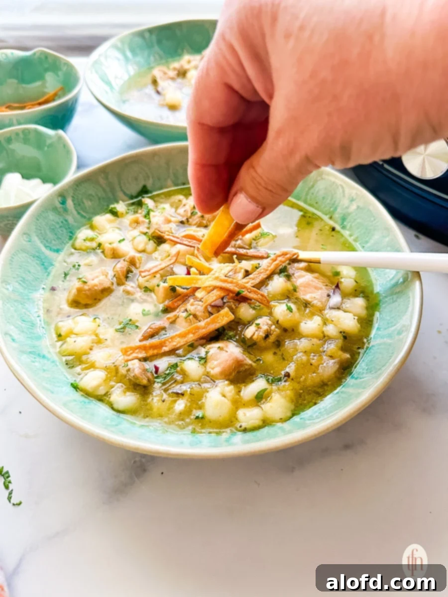 Speedy Instant Pot Pozole 9 A close-up shot of a hand garnishing a bowl of Instant Pot Chicken Pozole with vibrant green cilantro and crispy tortilla strips, emphasizing the fresh toppings.
