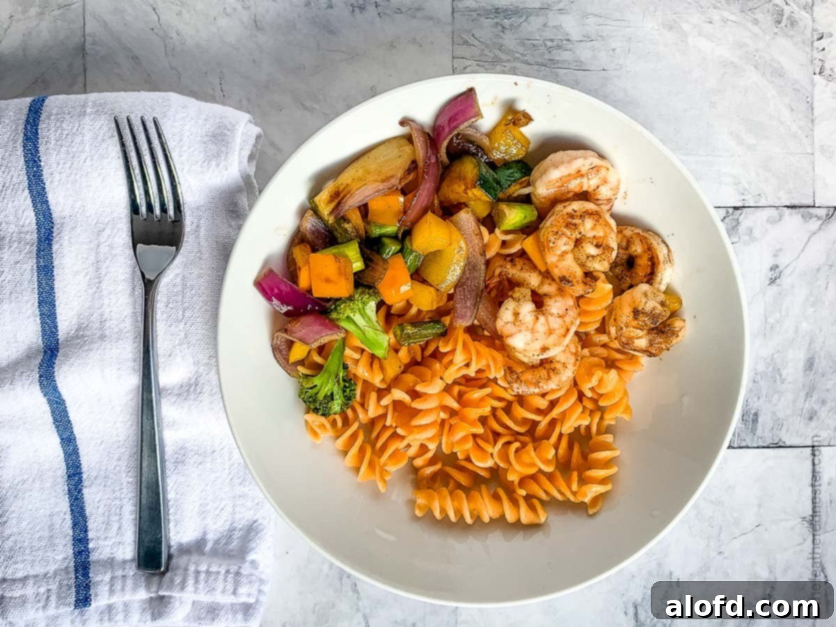 Vibrant Blackstone Veggies 8 A tantalizing spread featuring grilled shrimp, rotini pasta, and a generous portion of crisp griddle-cooked vegetables on a white plate, showcasing a healthy and delicious meal.
