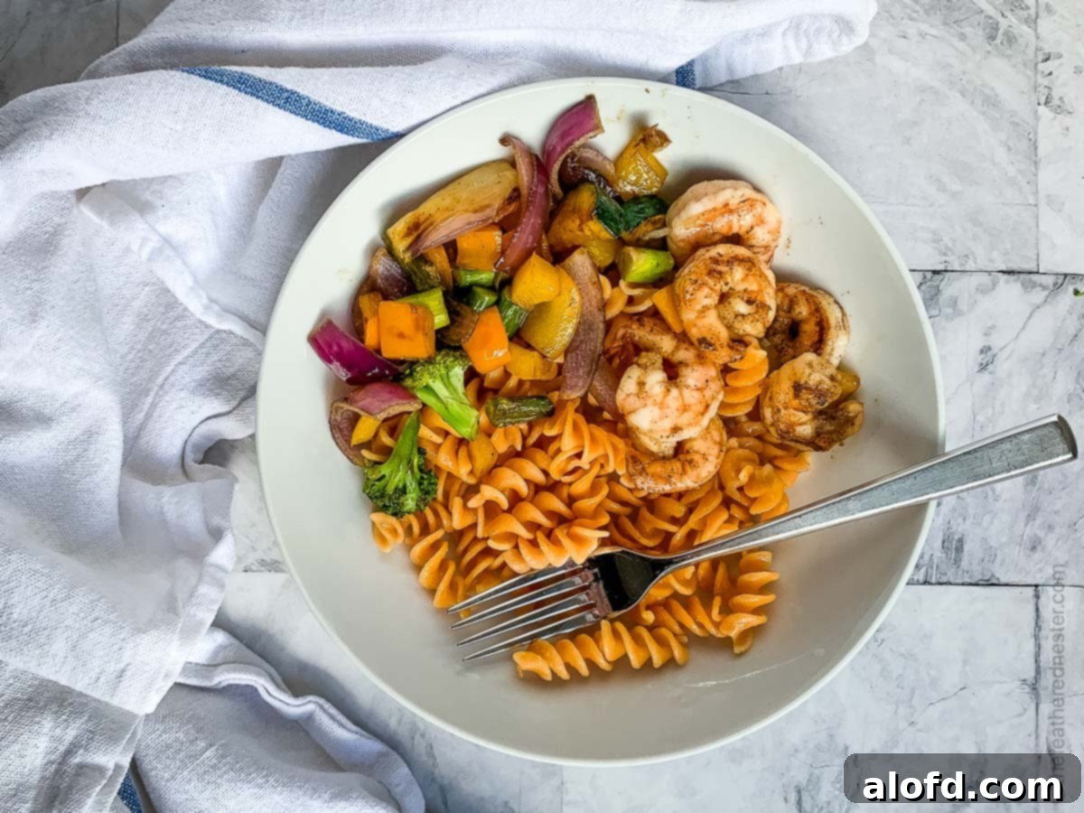 Vibrant Blackstone Veggies 9 A white plate featuring grilled vegetables, rotini pasta, and shrimp, arranged artfully after being cooked on a flat top grill.