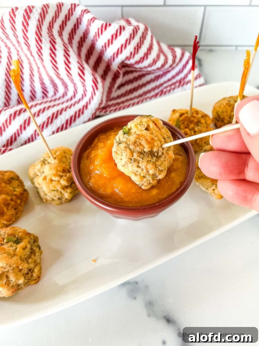 A bowl of vibrant mango sweet chili sauce with a crispy sausage ball being dipped into it, presented on a white serving tray with a decorative red and white napkin.