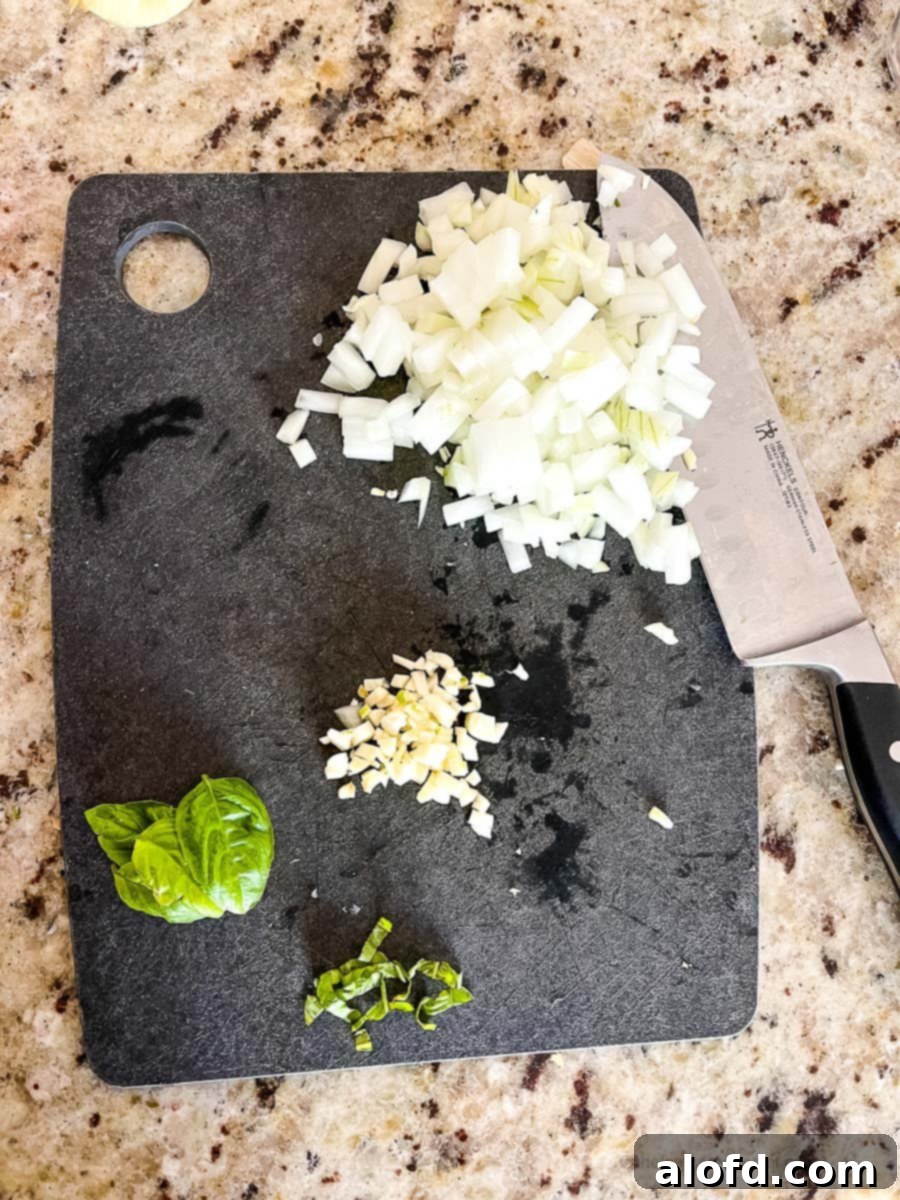 Instant Pot Creamy Tortellini Soup 5 Chopped onions, garlic and basil leaf on top of a black chopping board with a knife.
