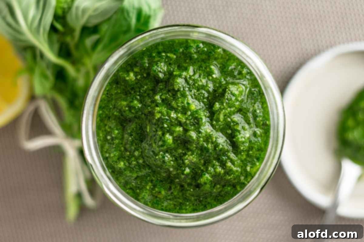 A jar of pesto sauce with a bunch of fresh basil and a rustic plate in the background.