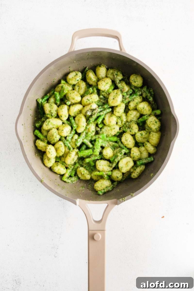 Looking down into a saucepan full of vibrant asparagus gnocchi coated in pesto sauce.