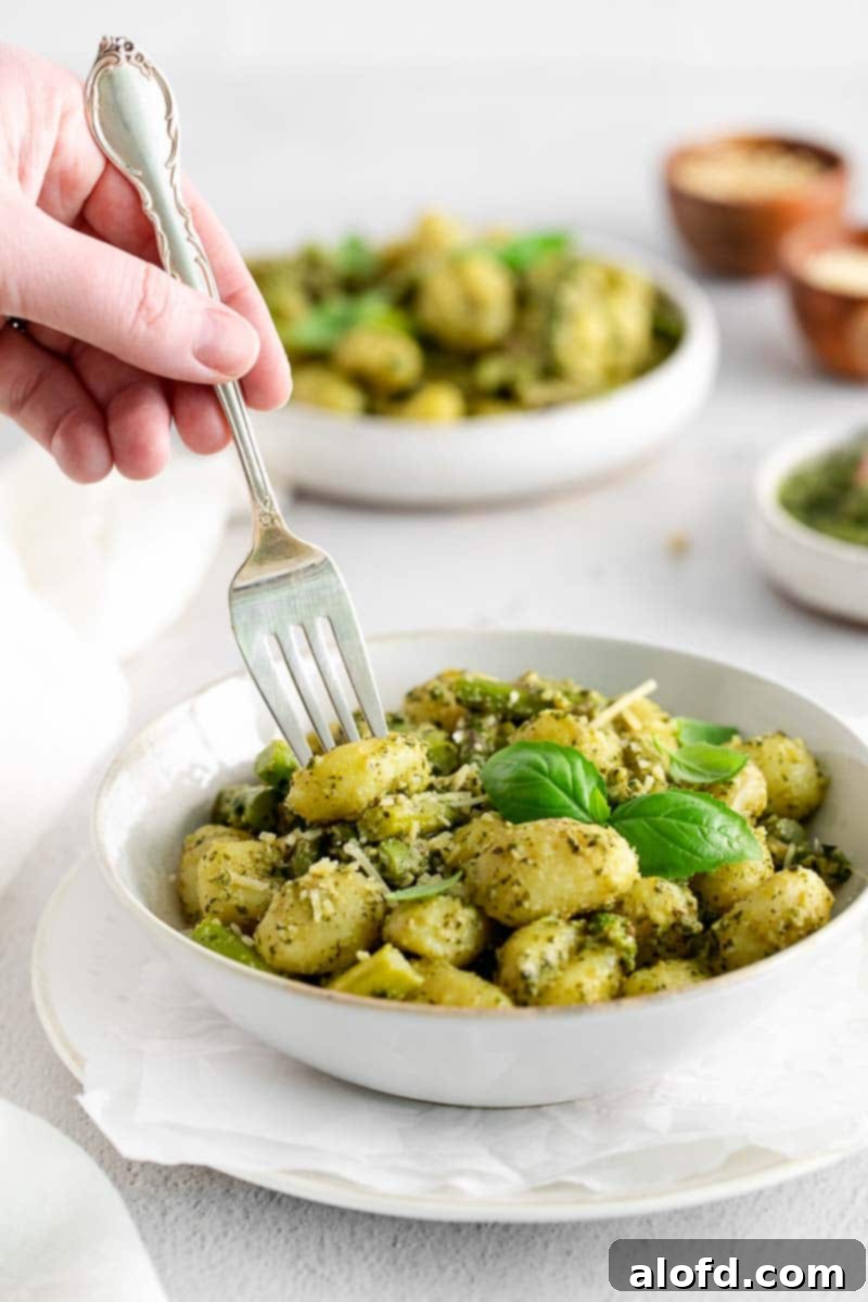 Woman's hand holding a fork in a bowl of pesto gnocchi, ready to eat.