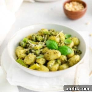 A white bowl of gnocchi and asparagus with a small bowl of parmesan cheese in the background.