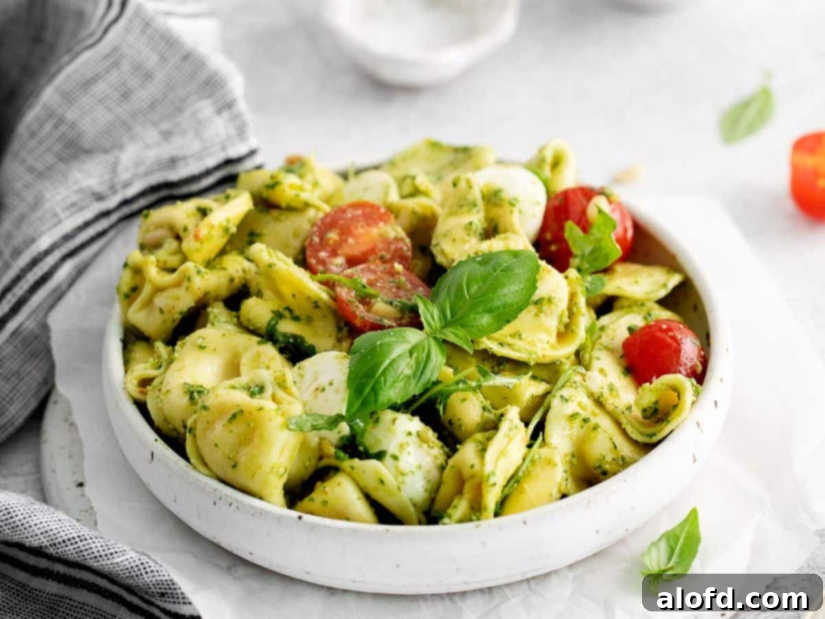 Pesto Tortellini Perfection 3 Tortellini, cherry tomatoes, and mozzarella balls, all covered with pesto sauce in a white pasta bowl.