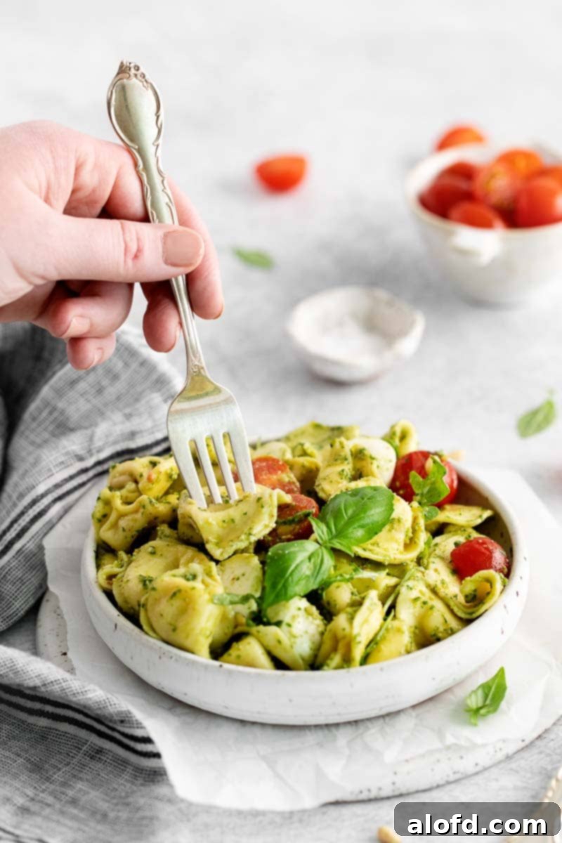 Pesto Tortellini Perfection 8 Hand holding a fork in a bowl of tortellini wtih pesto sauce.