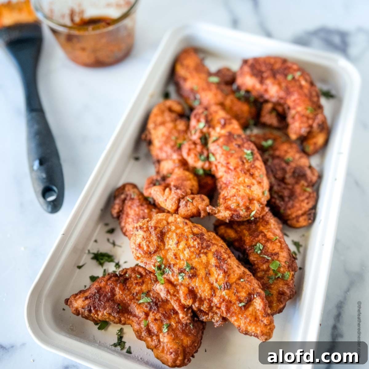 Fiery Nashville Chicken Strips 2 A white serving platter of fried chicken with a basting brush and spicy hot butter sauce in the background.