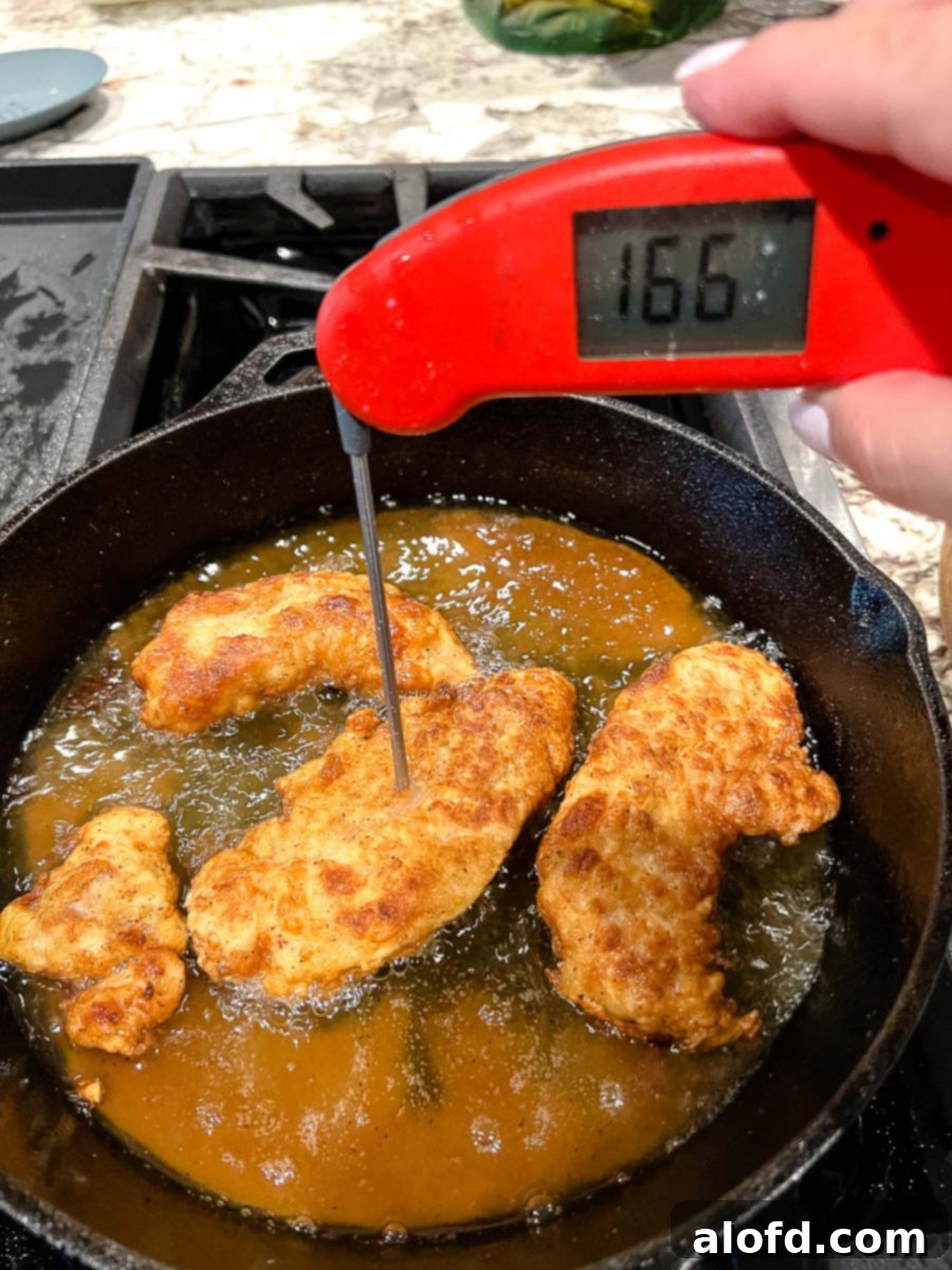 Fiery Nashville Chicken Strips 9 Frying the chicken strips in a cast iron skillet with a instant read thermometer showing the temperature of 166 degree Fahrenheit.