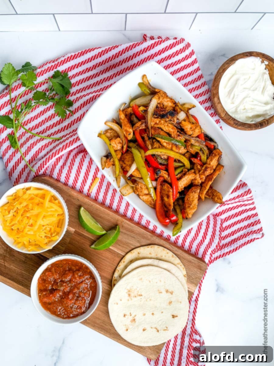 A inviting white bowl brimming with perfectly cooked chicken fajitas, surrounded by individual bowls of shredded cheese, fresh salsa, cool sour cream, and a stack of warm flour tortillas. This feast is beautifully arranged on a wooden board atop a red and white checkered cloth, showcasing the ultimate spread for a delicious and easy Blackstone Chicken Fajitas meal.