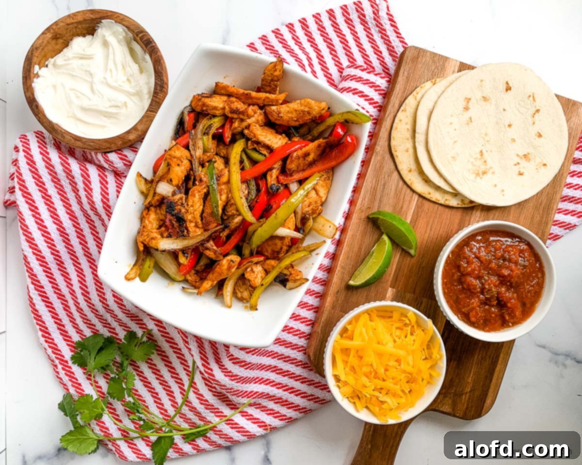 A beautifully presented bowl of Blackstone chicken fajitas, accompanied by warm flour tortillas, a vibrant bowl of salsa, a generous serving of shredded cheese, and a fresh lime wedge, all artfully arranged on a rustic wooden board over a red and white checkered cloth.