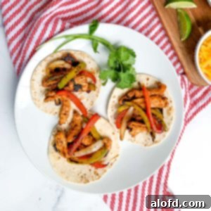 A plate featuring three succulent Blackstone chicken fajitas on flour tortillas, garnished with a sprig of cilantro, presented on a white plate with a red and white napkin.